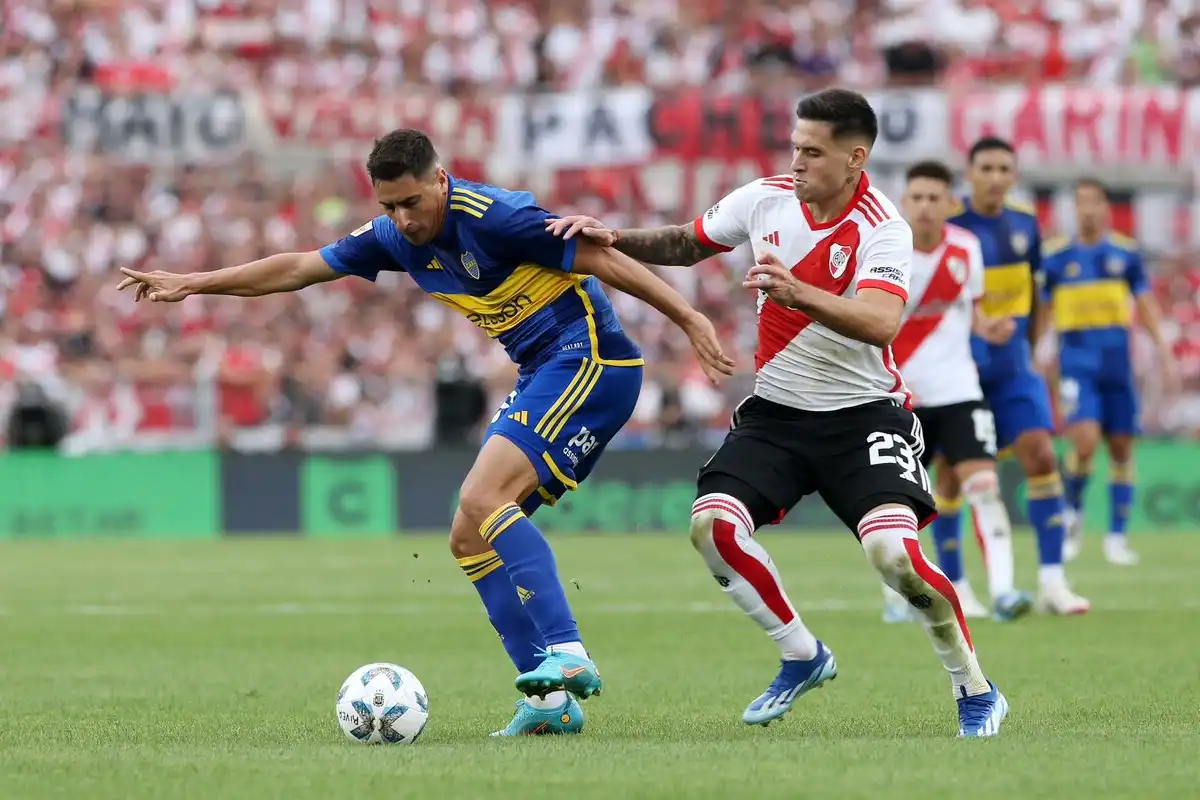 Jugador de boca pateando la pelota y jugador de river corriéndolo
